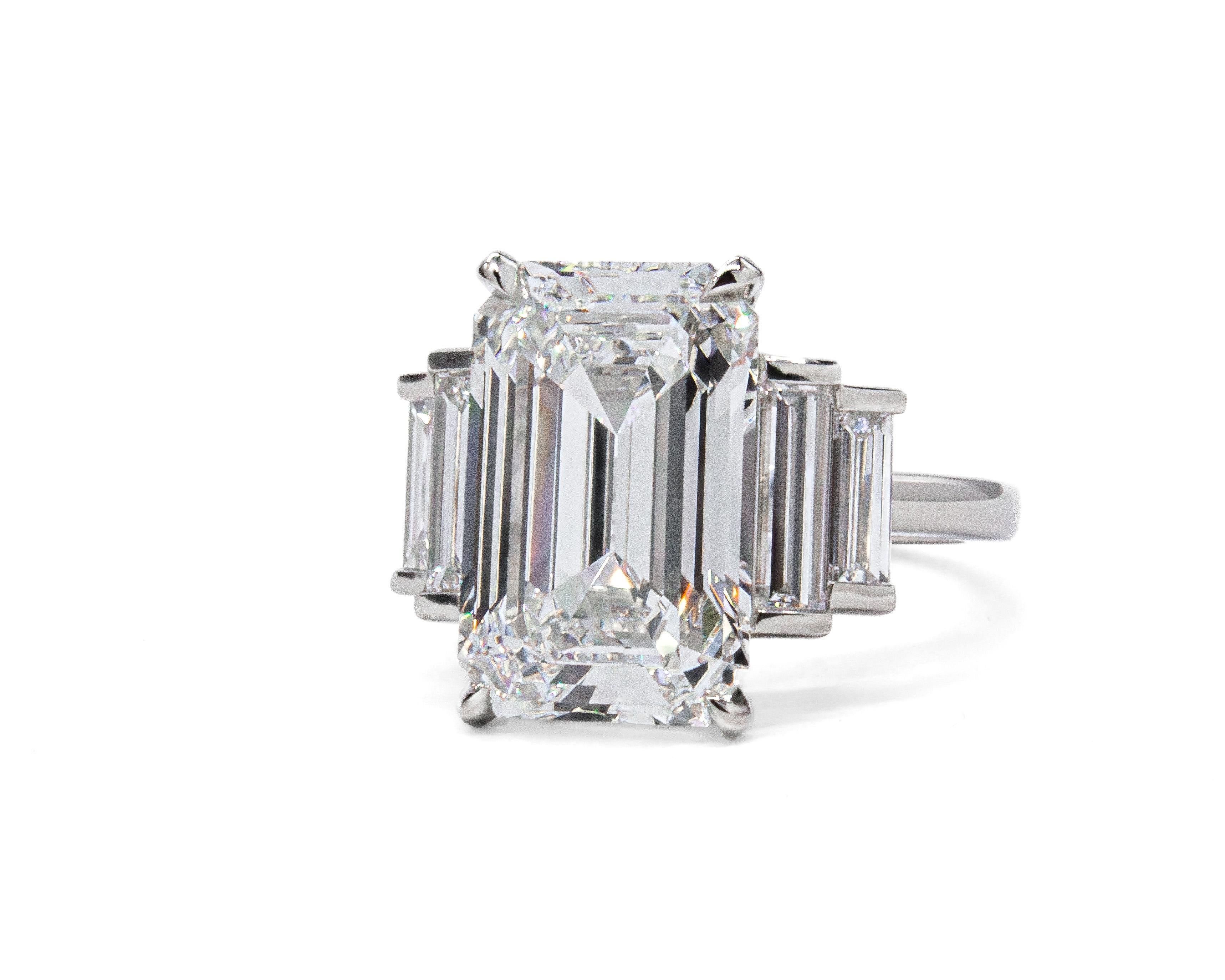 Questo elegante anello in platino a cinque pietre presenta al centro uno splendido diamante taglio smeraldo da 7,03 carati, certificato da GIA con colore E e purezza VS1. Eccezionalmente luminosa e di bellissime proporzioni, la pietra centrale è un
