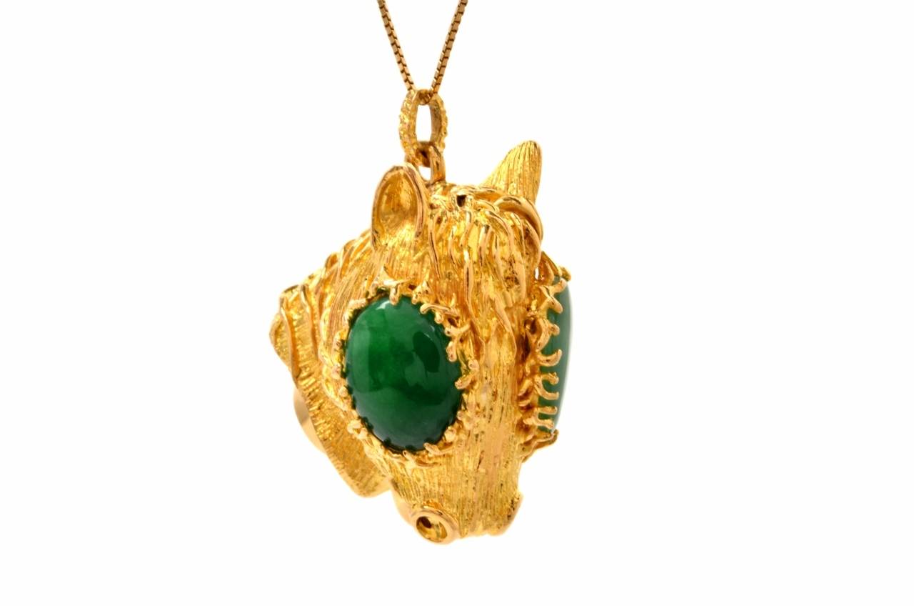 This pendant of rare and creative design simulates the stylized,  sculptured head of a llama, rendered in artfully textured 18K yellow gold. The animal's large eyes are simulated by a duo of genuine jadeite oval cabochons, cumulatively weighing