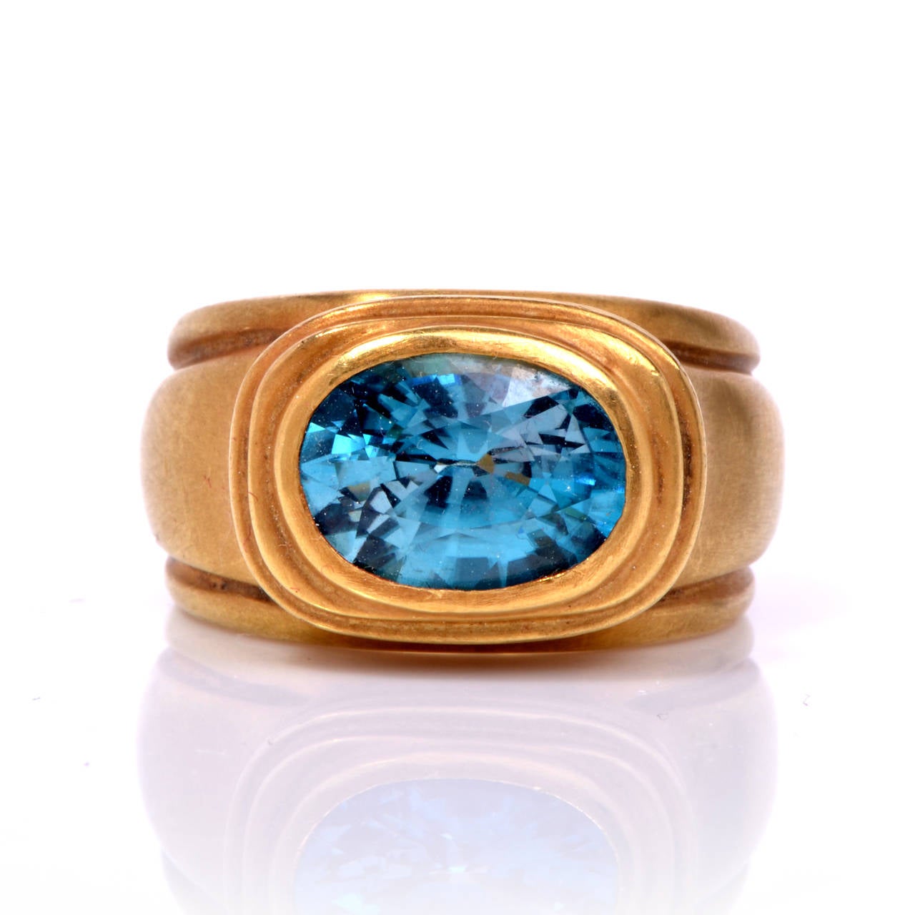 This mesmerizing and substantial ring is a truly exquisite creation. Finely crafted in solid 18K greenish yellow gold, it features a bezel set genuine oval cut blue zircon approx. 5.00ct. The gleaming and colorful center stone is complimented by the