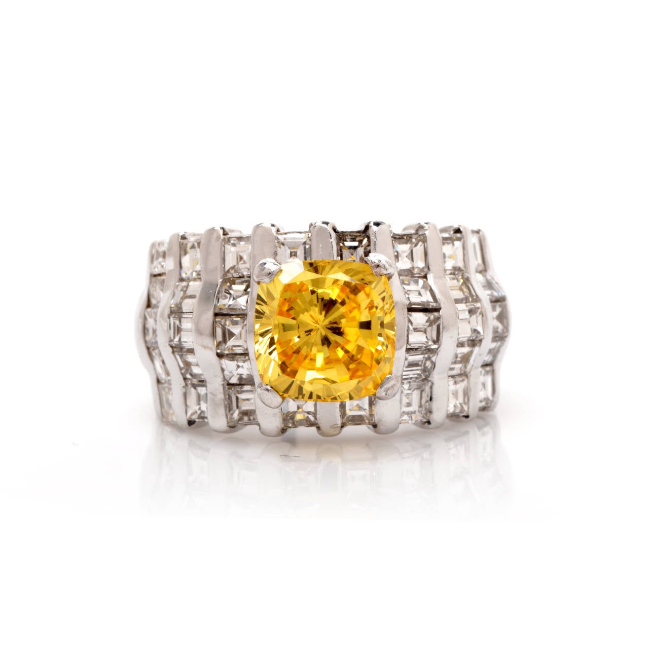 This estate ring with a cushion-cut yellow sapphire and baguette-cut diamonds is crafted in solid 18K white gold and weighs approx. 15.2 grams. Designed as a classically distinct wide band, this eye-catching estate engagement ring exposes at the