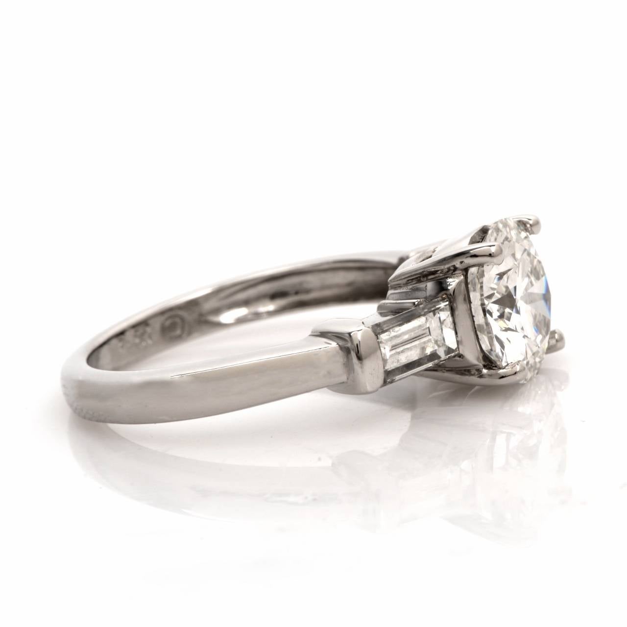 This classically distinct estate engagement ring with a round brilliant-cut and a pair of baguette diamonds is crafted in solid platinum and weighs approx. 3.67 grams. Designed with  quintessentially vintage characteristics, this alluring engagement