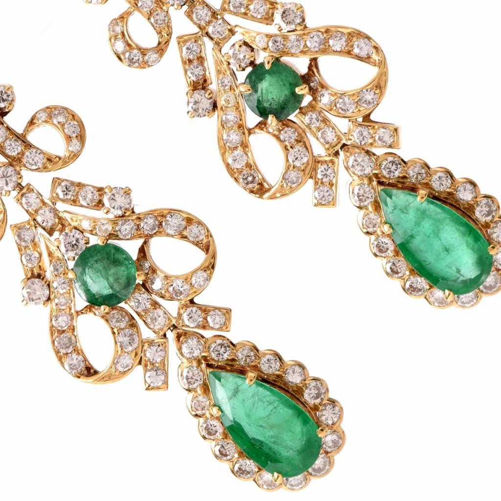 These vintage retro chandelier earrings crafted in 18K yellow gold expose ech a pear-shape faceted emerald within a diamond-studded pear-shape frame, surmounted by delicate scrolls enriched with two round-gfaceted emeralds and round-faceted diamonds