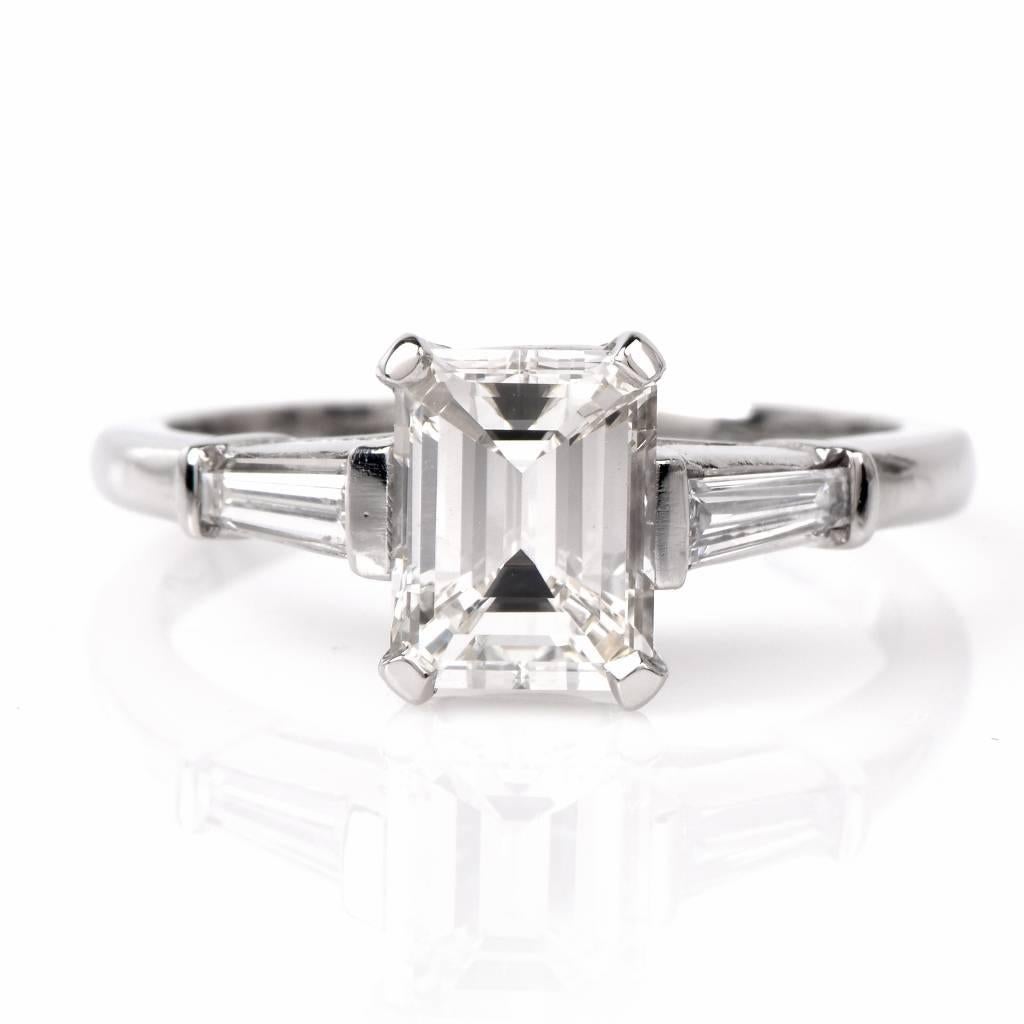 This vintage engagement ring of feminine grace is crafted in solid platinum and exposes at the center a 1.51ct genuine emerald-cut diamond graded I color and VS clarity. The center stone is flanked by a pair of tapered baguette diamonds with a total