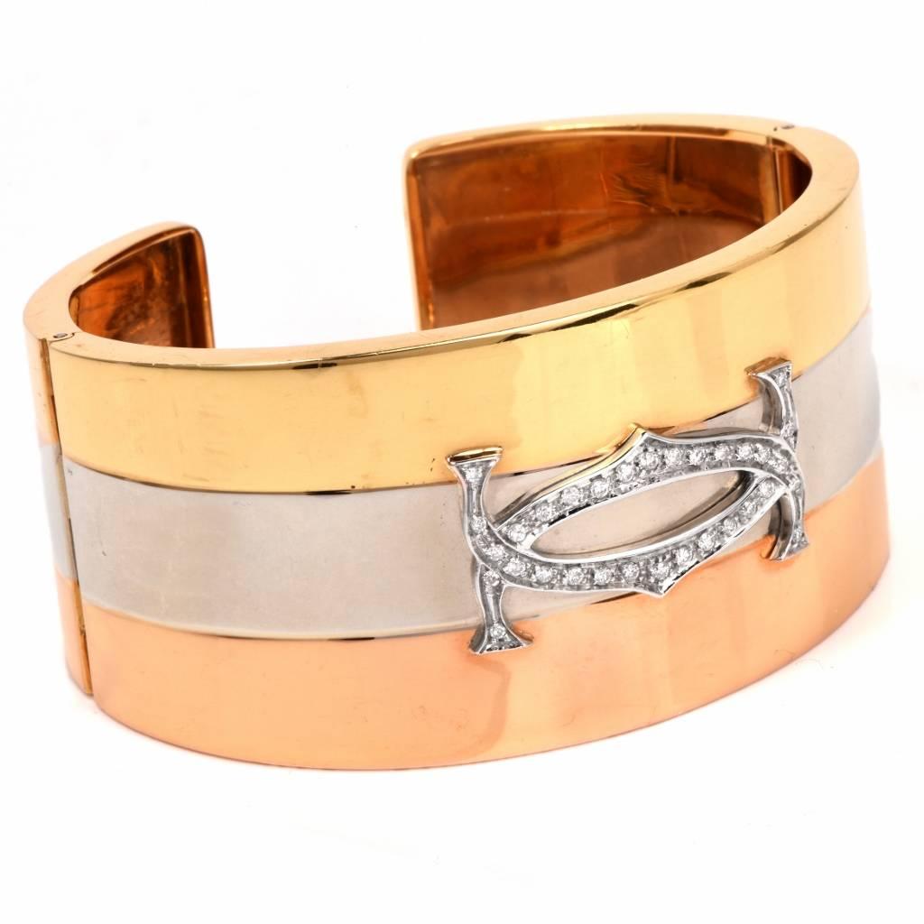 Rendered in tri-tone 18K gold with three horizontal stripes and delicate side hinges, this circa 1980's cuff bracelet is embellished with high polished gold and a fine diamond-studded decor of stylized oblong format at the center, set with 0.30ct of