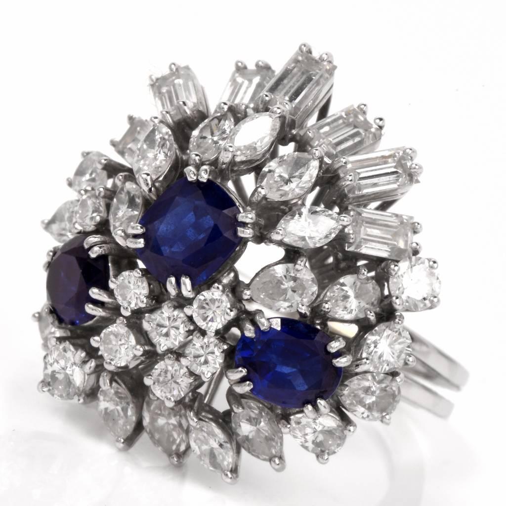 This cocktail ring circa 1960's, is handcrafted in solid 18K white gold with an assemblage of genuine blue sapphires and variously cut diamonds. The three oval-faceted royal blue sapphires weigh cumulatively 2.70cts. They are complemented by 11