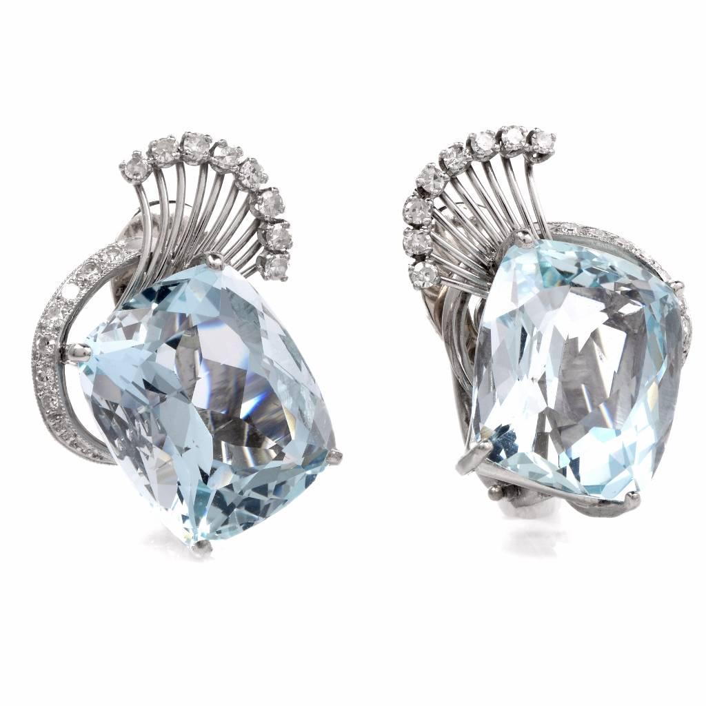 These aquamarine opulent earrings of  Retro era are crafted in 18K white gold.  They expose each an enchanting rectangular cushion-cut  aquamarine, cumulatively weighing 34.18 carats. The translucent precious gemstones are complemented  by a total