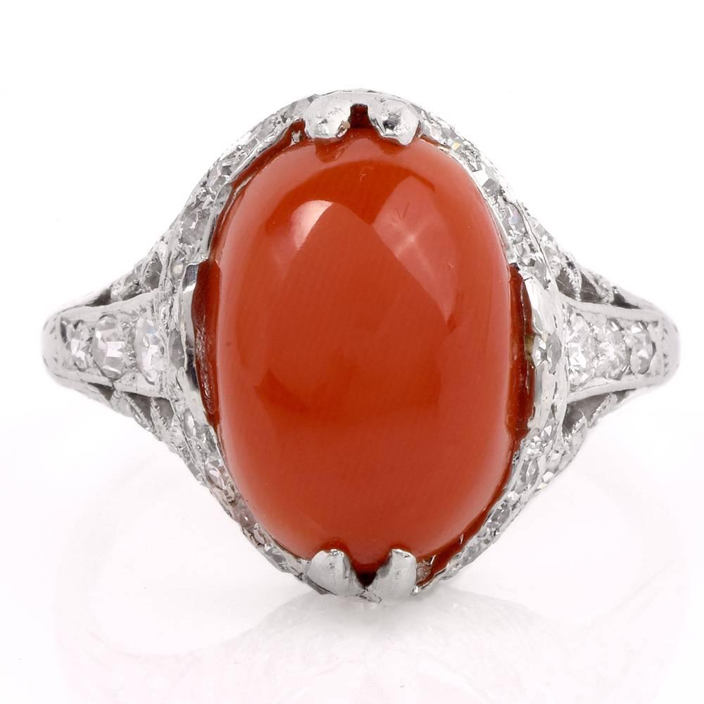 This antique Art Deco ring is crafted in solid platinum and exposes a genuine oval cabochon natural red coral at the center approx: 14mm x 11mm. Secured by paw-prongs, the eye-catching red coral is mounted atop a diamond-studded, elaborately