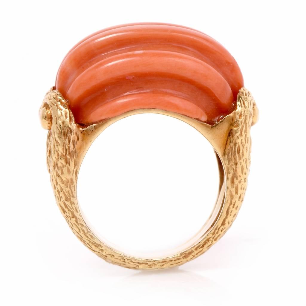 This elegant vintage  ring is crafted in solid 18K yellow gold. This unique ring exposes a genuine carved salmon colored coral stone. The band features a scroll design with a textured finish. This beautiful vintage coral ring remains in excellent