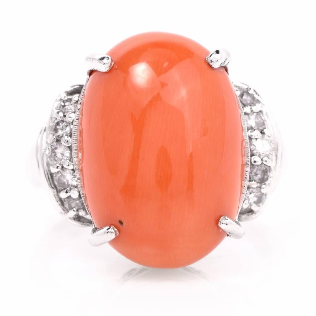 This opulent estate cocktail ring is crafted in solid platinum. It is centered with a carved coral cabochon of a popular salmon color, measuring 19mm x 13.5mm secured by 4 prongs, surrounded by 10 round-faceted diamonds adorning the broad shoulders,