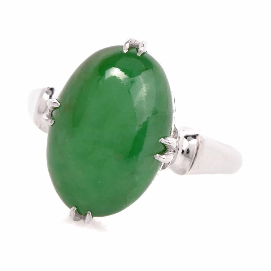 This ring of elegant simplicity is crafted in platinum and exposes a solitaire green jade oval cabochon, weighing 6.04cts, secured by four delicate paw-prongs, the gemstone is placed atop an ornate, openwork gallery, flanked by tri-dimensional