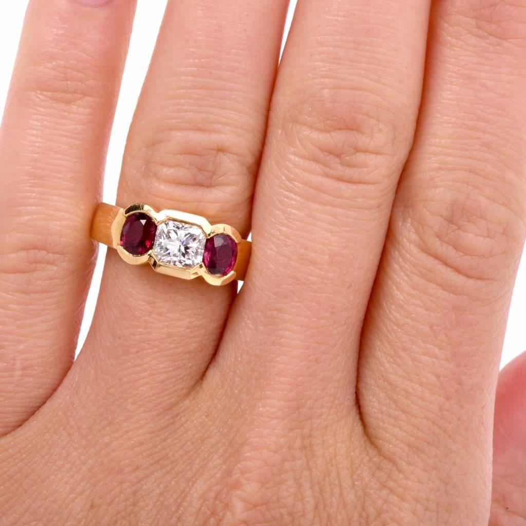 This alluring three-stone  ring is crafted in solid 18K yellow gold. This ring is centered with 1 genuine square brilliant- cut diamond weighing approx 1.02ct, graded G-H color and VS1 clarity. It is accented with some 2 genuine round rubies of