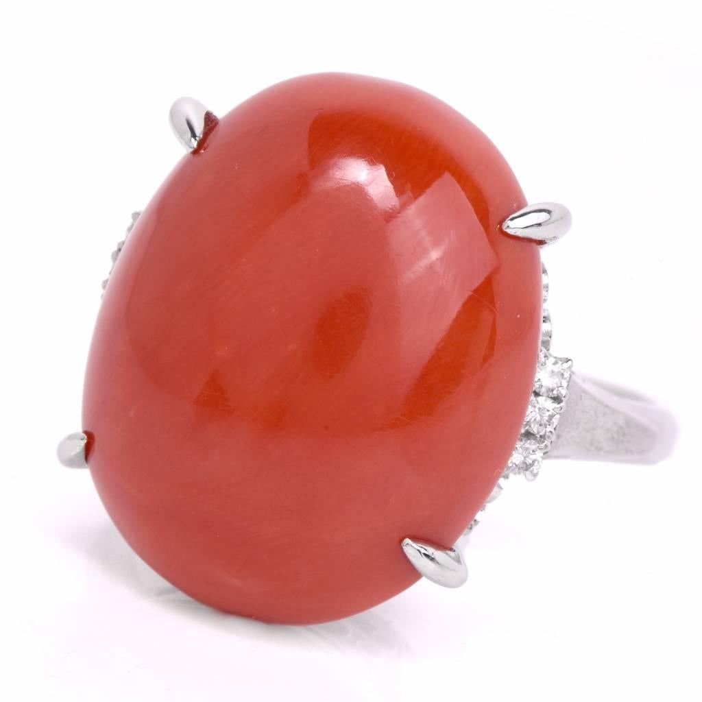 This opulent1960's cocktail ring is crafted in solid platinum. It is centered with a carved coral cabochon of a natural red salmon color, weighing 20.2 carats, measuring 21mm x 17.5 mm secured by 4 prongs, surrounded by 6 round-faceted diamonds