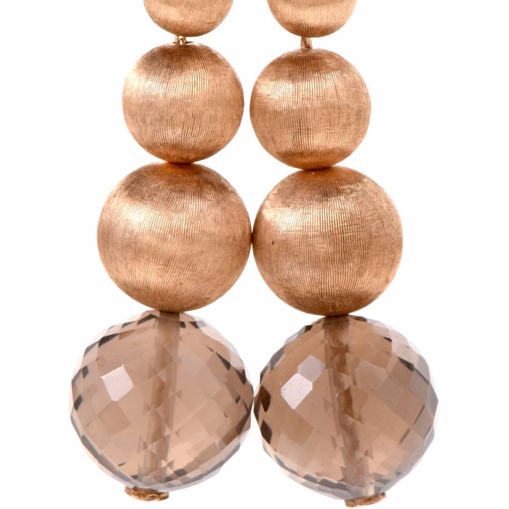 These  pendant earrings are crafted in 14Karat yellow gold, weighing 5.9 grams and measuring 1.7 inches long. They comprise each a faceted and drilled smoky quartz bead surmounted by 4 graduated gold beads, with the two smallest constituting the ear