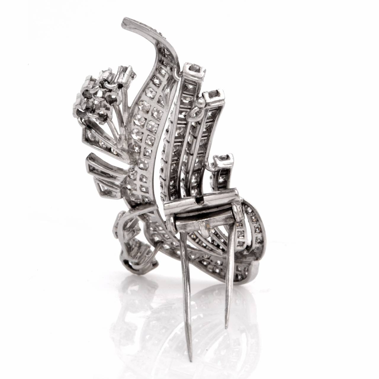 This antique lapel brooch with diamonds is crafted in solid platinum, weighing 16.1 grams and measuring 60 x 20 mm.  Designed as a stylized floral motif brooch , simulating diamond-studded buds, leaves and gracefully curved  stems, this antique 