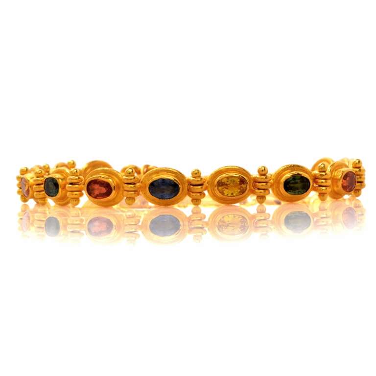 This gemstone designer bracelet is crafted in solid 23K yellow gold (purity 985) and features a total of 13 genuine oval cut multicolored sapphire gems approx: 4.68 cttw with vibrant vivid color, all bezel set in a flexible single line design. This