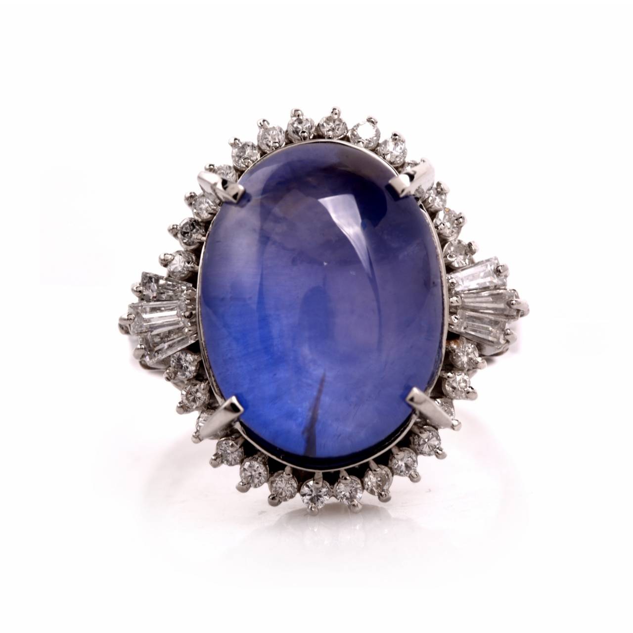 This stunning estate ring is crafted in solid platinum. Showcasing an impressive statement design that is centered with 1 genuine oval cabochon Natural No heat blue sapphire approx: 21.48cttw that is framed by 28 genuine round cut diamonds and  6