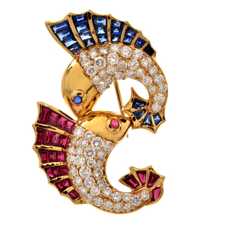 This vivacious lapel brooch pin incorporates a pair of fish adorned with rubies and blue sapphires on their dorsal fins, eyes and tails, while their scales are simulated by pave diamonds. Artfully juxtaposed to face each other, the enchanting 