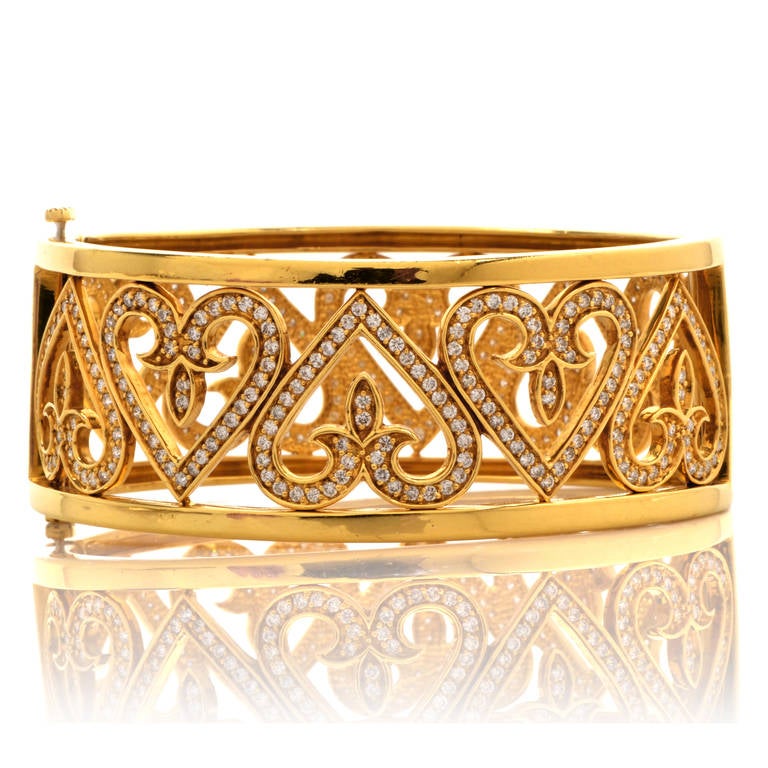 This magnificent bangle bracelet is crafted in solid 18K yellow gold. This piece showcases a heart motif enhanced with some 390 genuine round cut dazzling diamonds approx: 4.50 cttw, H-I color, VS clarity, pavé set. With a center hinge and a
