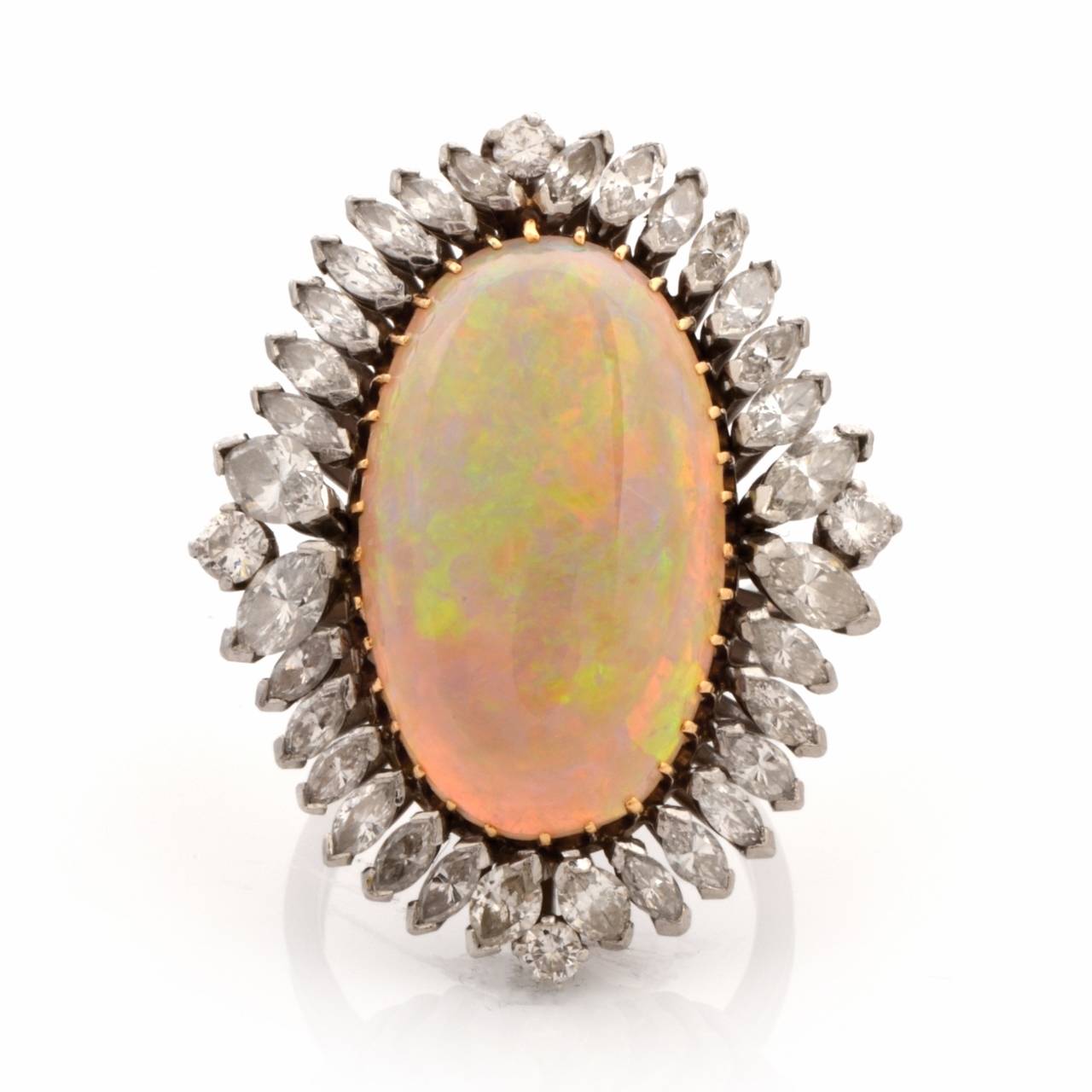 This conspicuous vintage ring with an oval-cut opal cabochon and marquise diamonds is crafted in platinum and weighs approximately 15.6 grams.  Incorporating an aesthetically alluring ovular plaque, it is centered  with an eye-catching fine opal