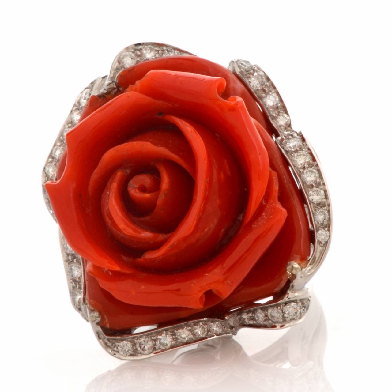 This Retro diamond and coral ring of opulent and captivating aesthetic is crafted in solid 18K gold, weighing 33.7 grams. Creatively designed as a red rose posed on diamond leaves, this fascinating ring exposes a masterfully carved  natural color