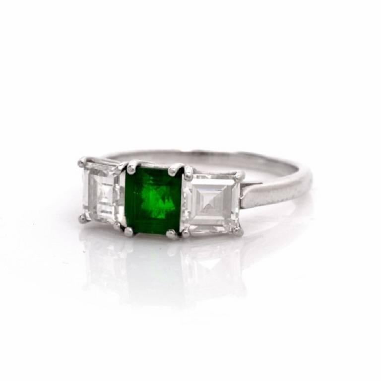This vintage three-stone engagement ring with an attention-seeking high  quality emerald-cut emerald  at the center is crafted in solid platinum and weighs approx.3.8 grams. This  engagement ring of timeless elegance  and enchanting aesthetic