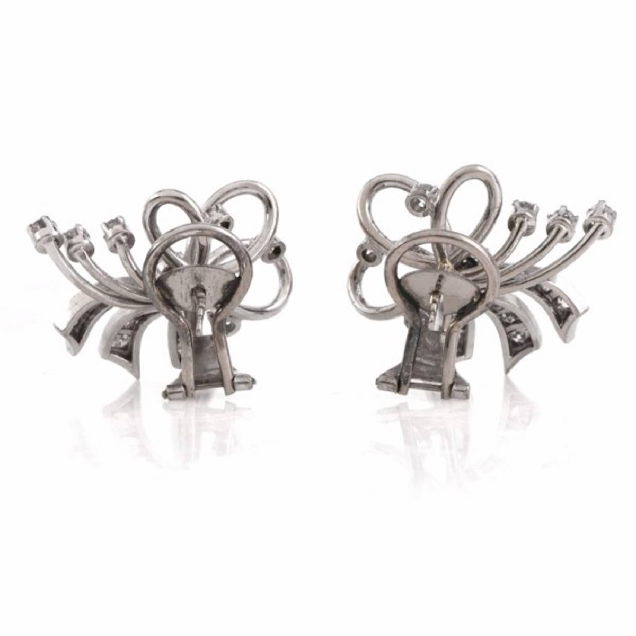 These enchanting vintage earrings depicting well designed swirl ribbon bow profiles are crafted in solid 18K white gold, weighing 9.6 grams and measuring 22 x 19 mm.These refined earrings of alluring monochromatic aesthetic are adorned with a total