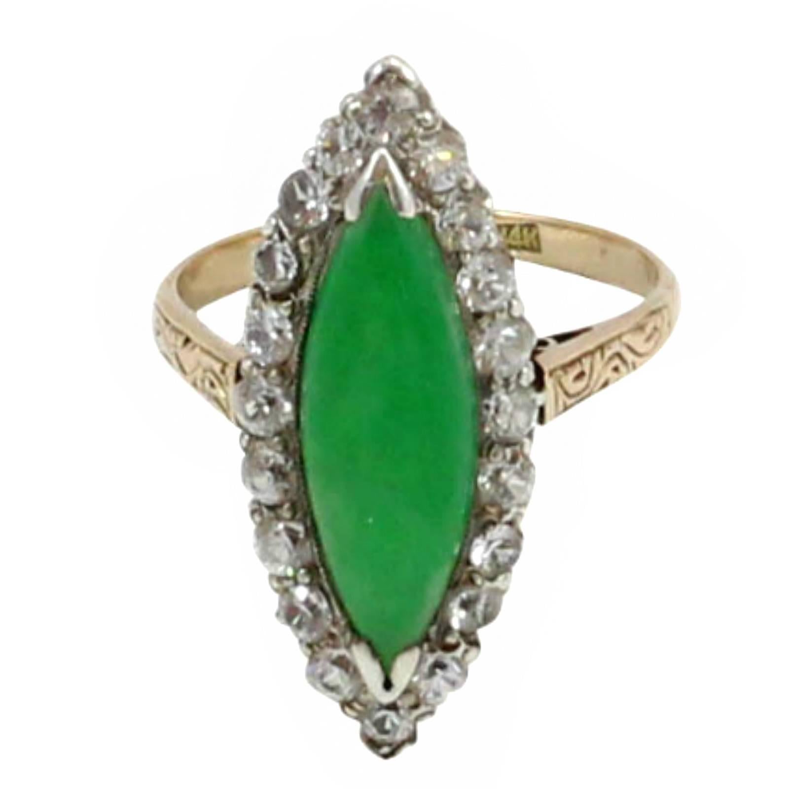 A handmade 14 karat gold ring, with a 1.95mm to 2.64mm wide rounded tapered shank and flow up engraved shoulders. The white gold cluster head contains one 18mm x 6.35mm marquise cabochon cut A Grade jadeite. It is surrounded by twenty 2.25mm