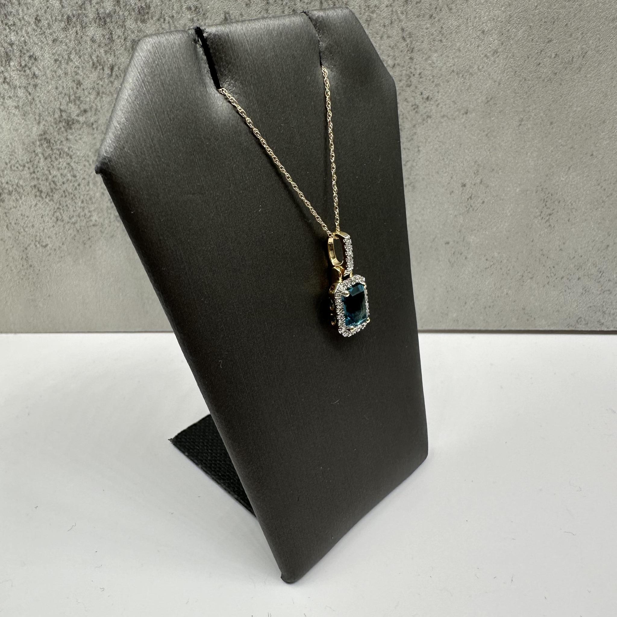 Cet élégant collier de topazes et de diamants en or jaune 10kt présente une superbe topaze bleue de Londres de 7x5 mm de taille émeraude, rehaussée de 0,11ctw de diamants ronds de taille unique GH SI naturels. Pesant seulement 1.6 gramme, il est