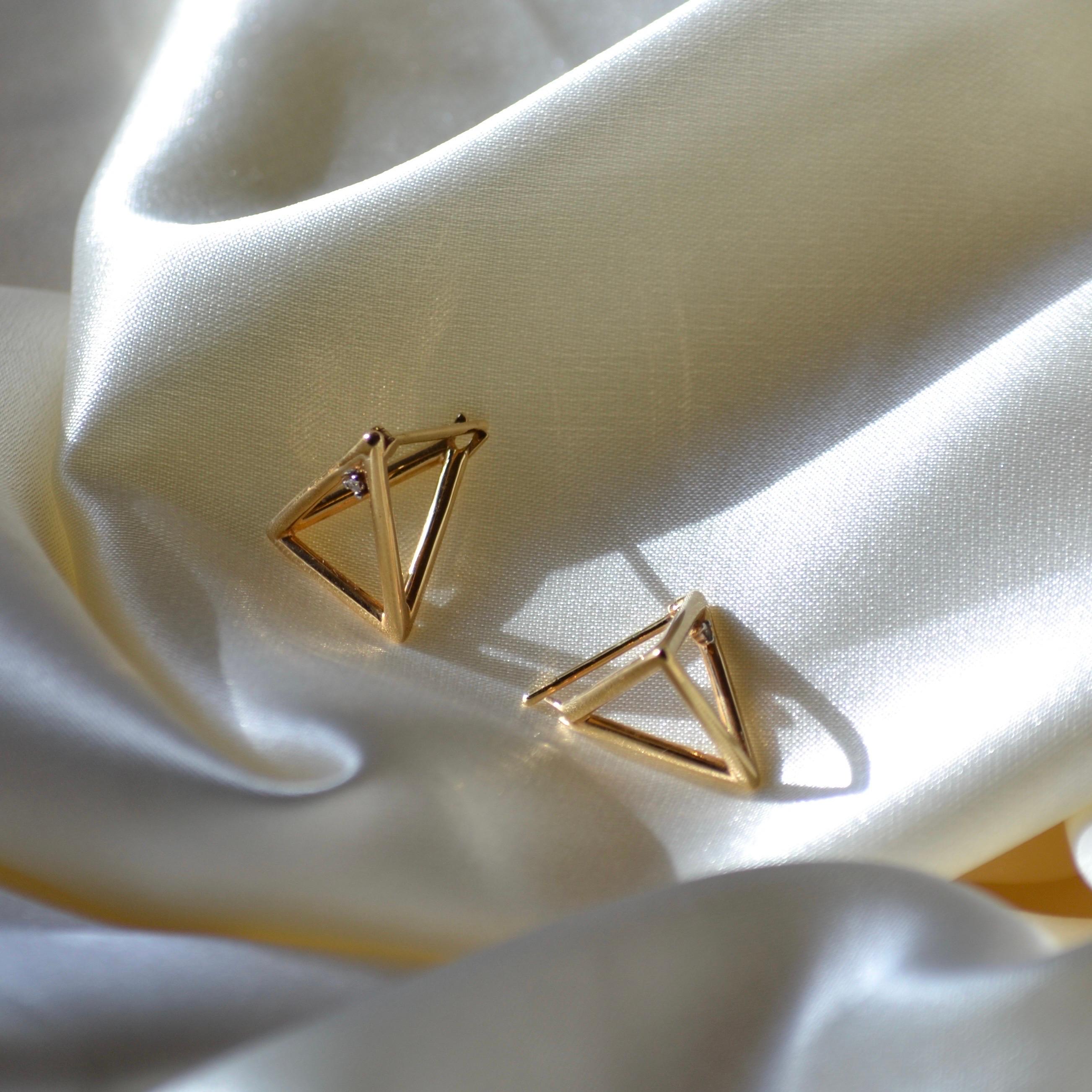 These stunning 18K yellow gold earrings bring modern geometry to life with a bold, three-dimensional pyramid design. The open-frame triangular shape creates a unique architectural style, enhanced by a single diamond accent on each earring, adding a