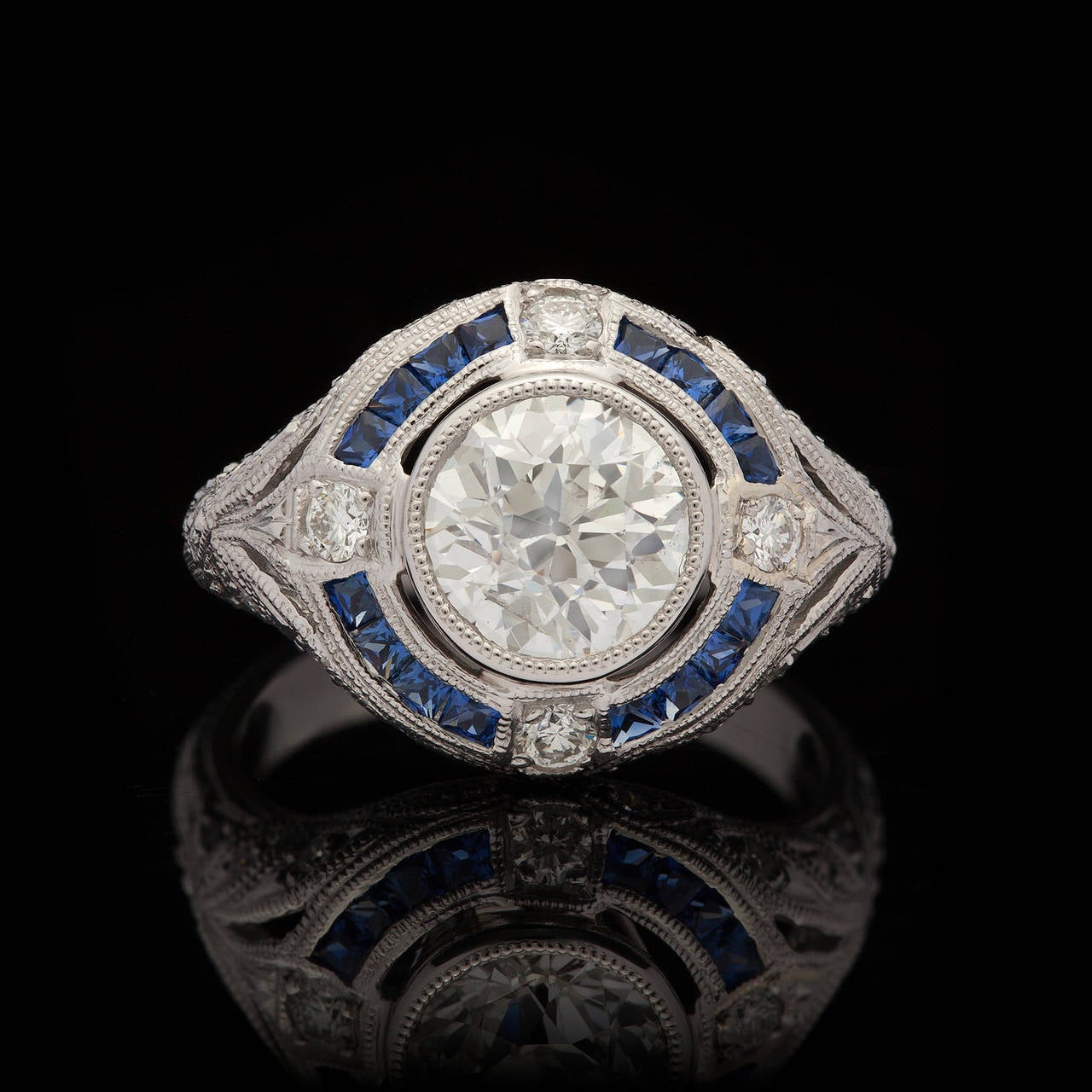 Platinum custom ring features one European cut J color, SI1 clarity diamond for a total approximate weight of 1.60cts, set with an additional 22 round cut diamonds for approximately 0.32cts and 16 blue sapphires for a total weight of 0.45cts. The