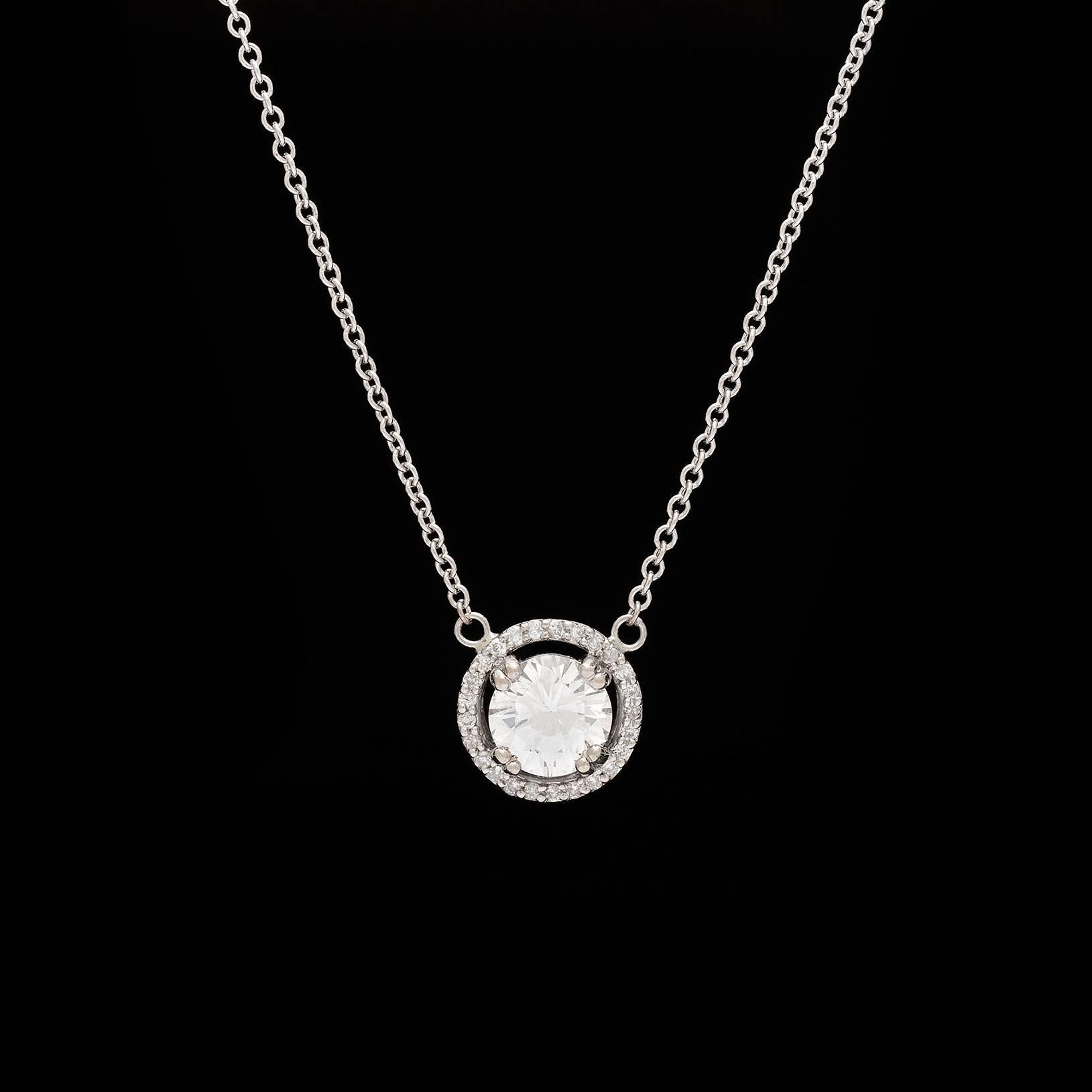 This 18k white gold diamond halo design pendant features a 0.95 carat round brilliant-cut diamond surrounded by 25 full-cut diamonds totaling 0.10 carats, with a length of 16 inches. The center diamond is G-H-I color and SI clarity. Nice added
