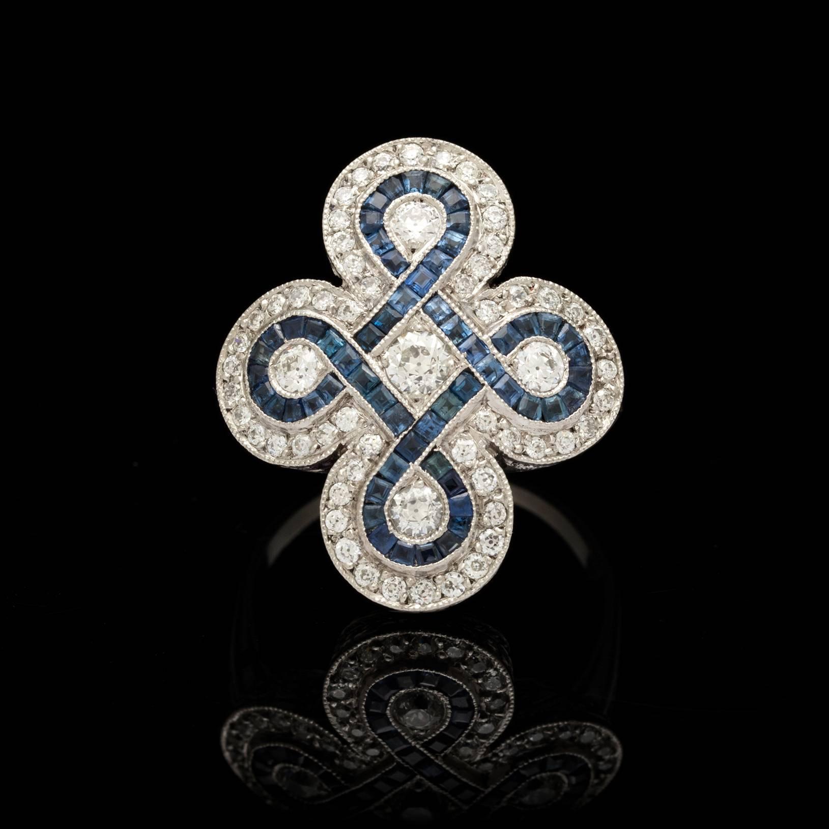 Deco style platinum ring features 5 old european cut diamonds totaling 0.40 carats. Surrounding these 5 diamonds in a swirl pattern are square cut sapphires detailed with 0.56 carats of old european diamonds along the border. Ring size is a 6.25 and