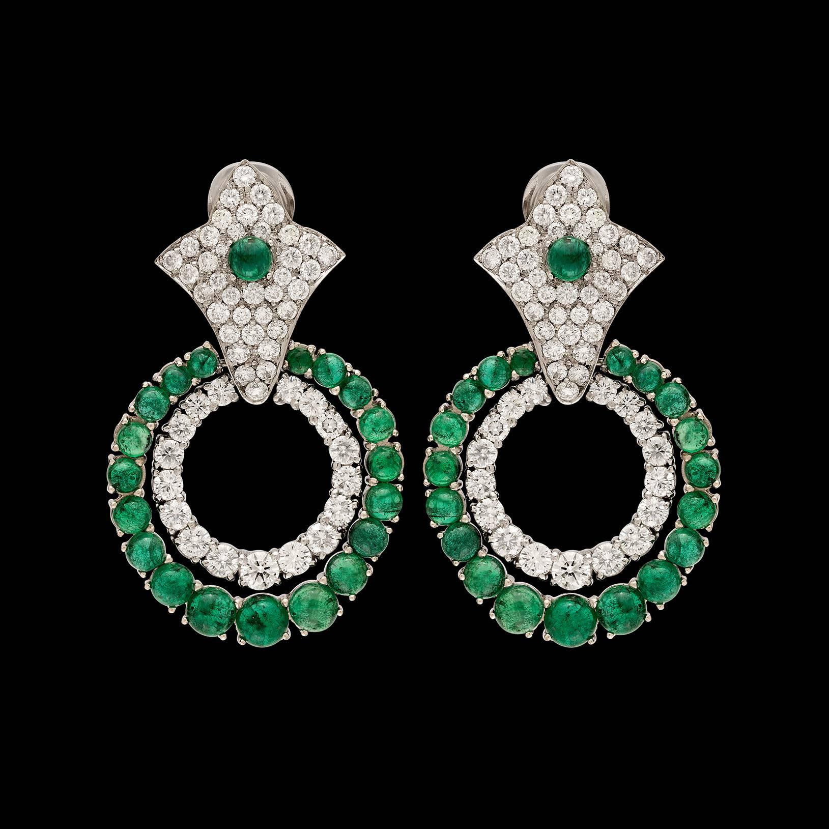 Fabulous 18k white gold doorknocker earrings are designed with shield-shaped tops with doorknocker circles, set throughout with 100 round brilliant-cut diamonds and 40 cabochon-cut emeralds. Total diamond weight is 6.50 carats, with a total emerald