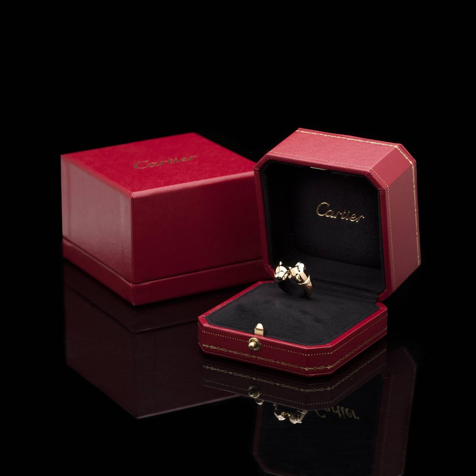 The must-have contemporary styling of a classic Cartier design, originally introduced in 1914. The 18k gold ring features facing panthers, tsavorite garnet eyes and onyx noses. The ring weighs 11.6 grams and is a size 5. With French marks and a