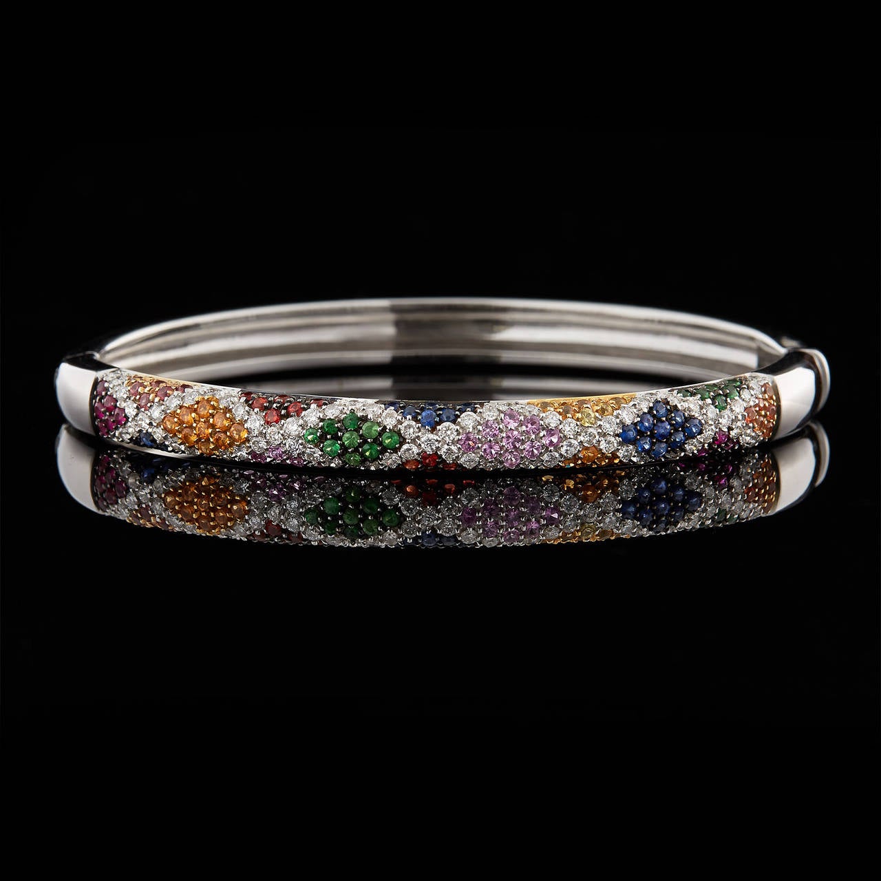 Salavetti 18Kt White Gold Bangle Pave Set with Colored-Stones in a Harlequin Pattern Design. The gemstones featured are 0.98 carats of blue sapphires, 0.18 carats of rubies, 0.45 carats of tsavorites, and 0.95 carats of diamonds. The bangle fits a