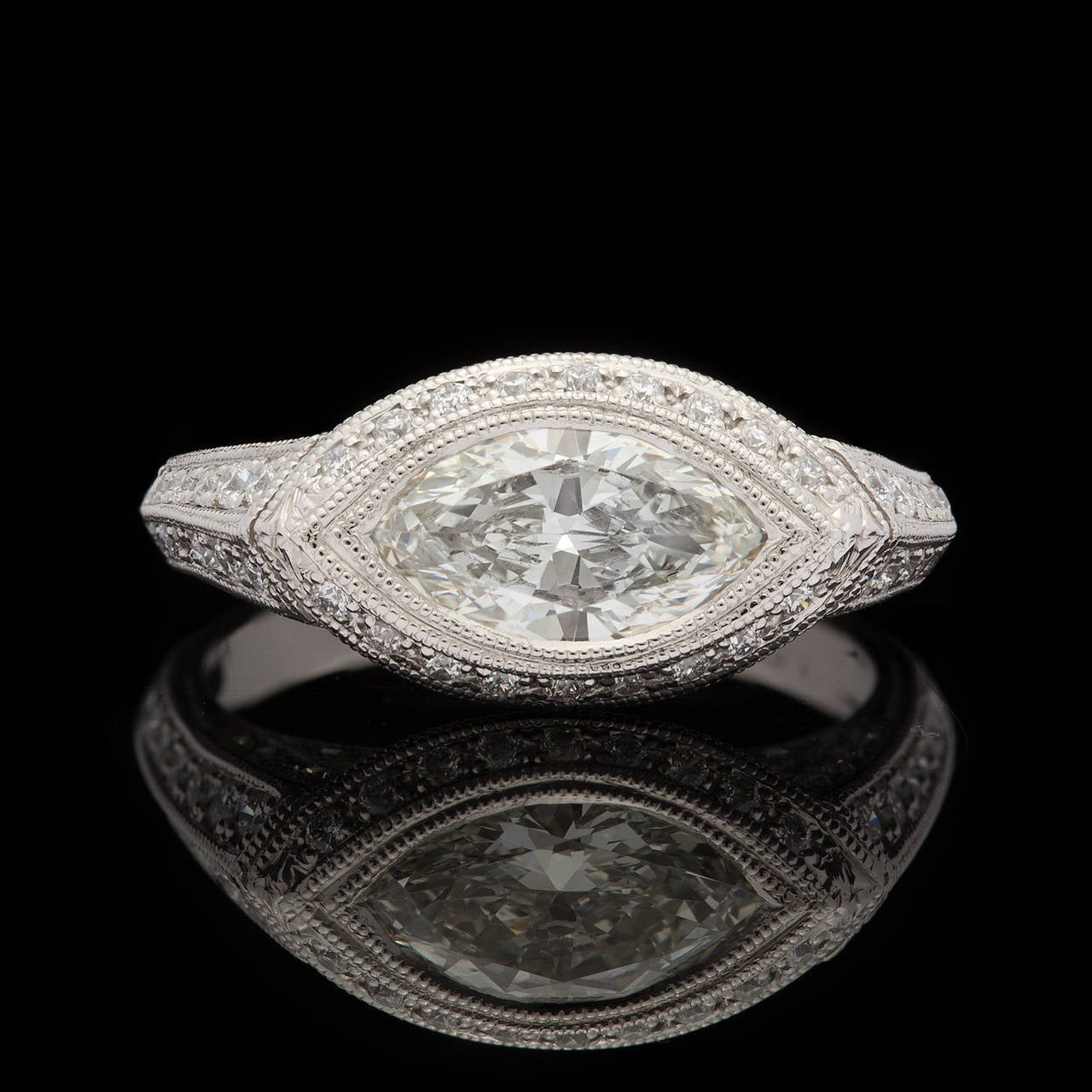 Custom Deco Style Diamond Ring features a 1.20 carat Marquise Cut Center Diamond Surrounded by 76 Round Brilliant Cut Diamonds totaling 0.50 carats set in Platinum. This marquise diamond is bezel set in a halo style weighing 6.3 grams & fits a size