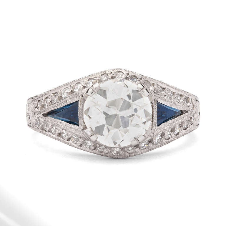 Platinum Ring features 1 European Cut K/SI1 Diamond for a total approximate weight of 1.73cts, set with an additional 38 round cut diamonds for approximately 0.45ct and 2 Faceted Triangle Cut Sapphires for a total weight of 0.40ct. The ring weighs
