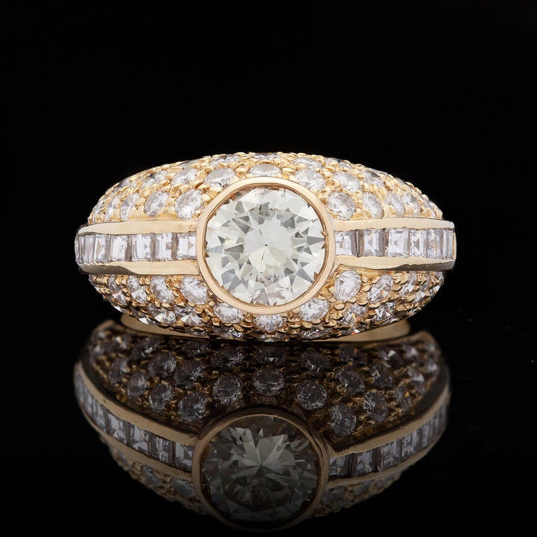 18Kt Yellow Gold Ring Features Round Brilliant Cut 1.15ct Diamond, with approximately J color and SI2 clarity. The ring is adorned with another 73 mixed cut diamonds for 2.25cts. The ring measures 11mm-4mm in width and is a size 6.5. The total
