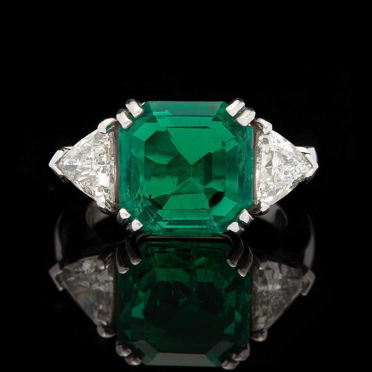 Platinum Ring with 5.40ct Green Square Emerald Cut Colombian Emerald Flanked by 2 Triangular Brilliant Cut Diamonds for approximately 1.20cts. The ring is a size 5.75 and weighs 10.7 grams. AGL report #CS 62144 is included.