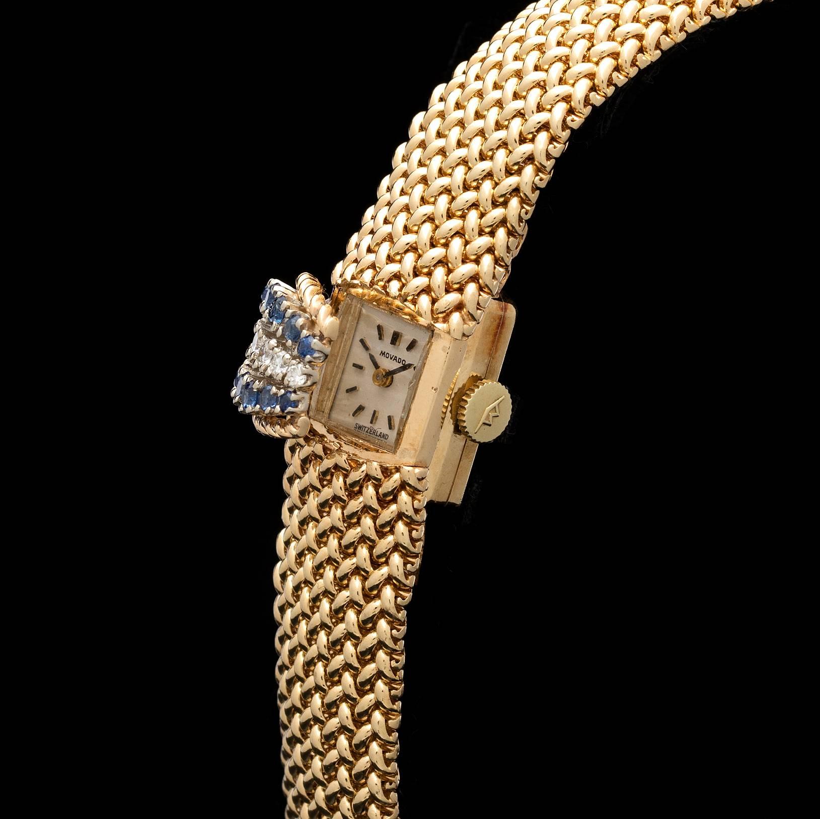 A fashionable 14k yellow gold vintage Movado timepiece with a manual wind Swiss movement.  The dial cover is adorned with 14 blue sapphires and 7 diamonds.  The mesh bracelet is 9/16 of an inch wide and 6 1/2 inches long.  This piece totals 39.1