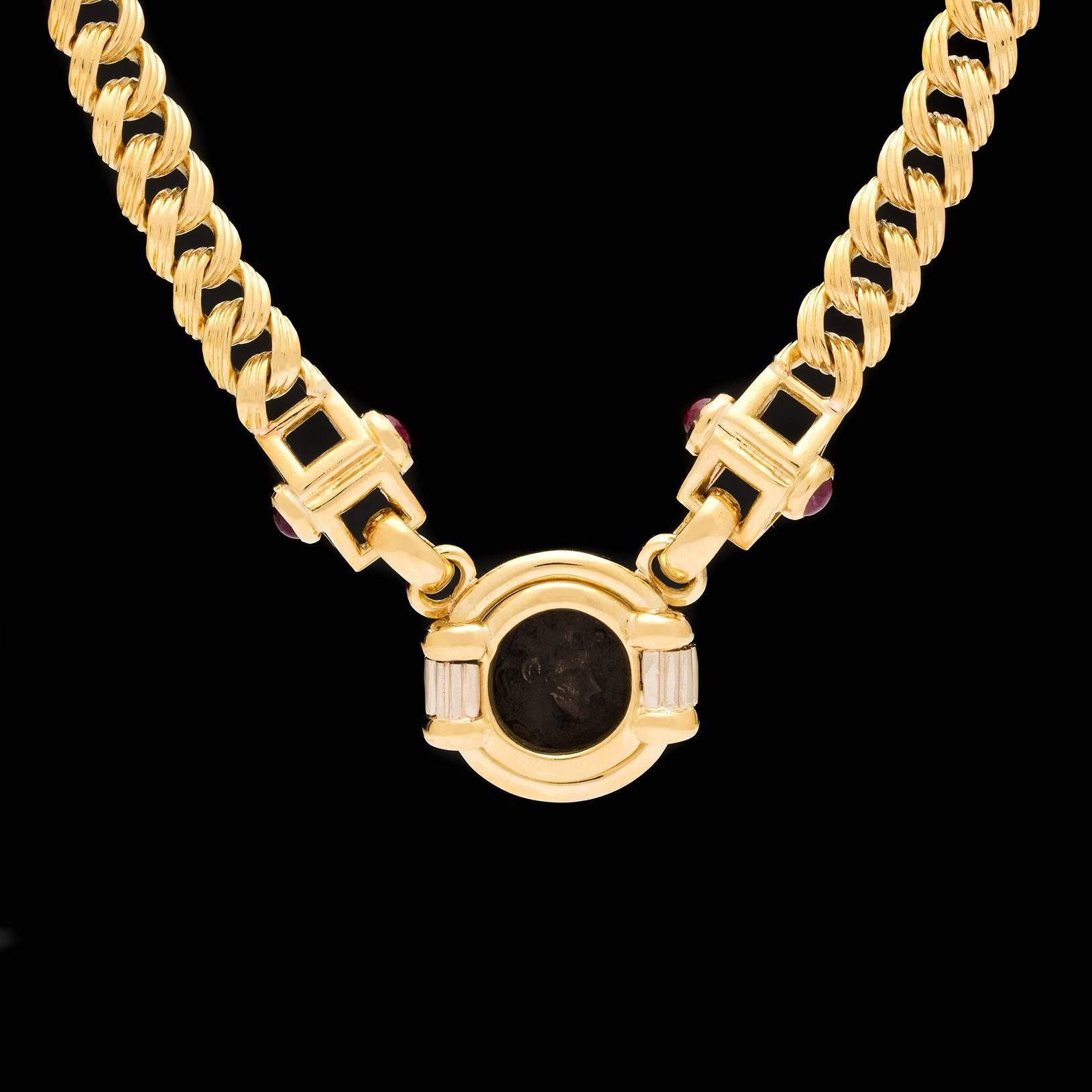 Estate 18k yellow gold necklace features a Roman Coin suspended by links detailed with 4 ruby cabochons on a two-toned textured flat curb link chain of 15 inches.  Total weight of the necklace is 53.1 grams.