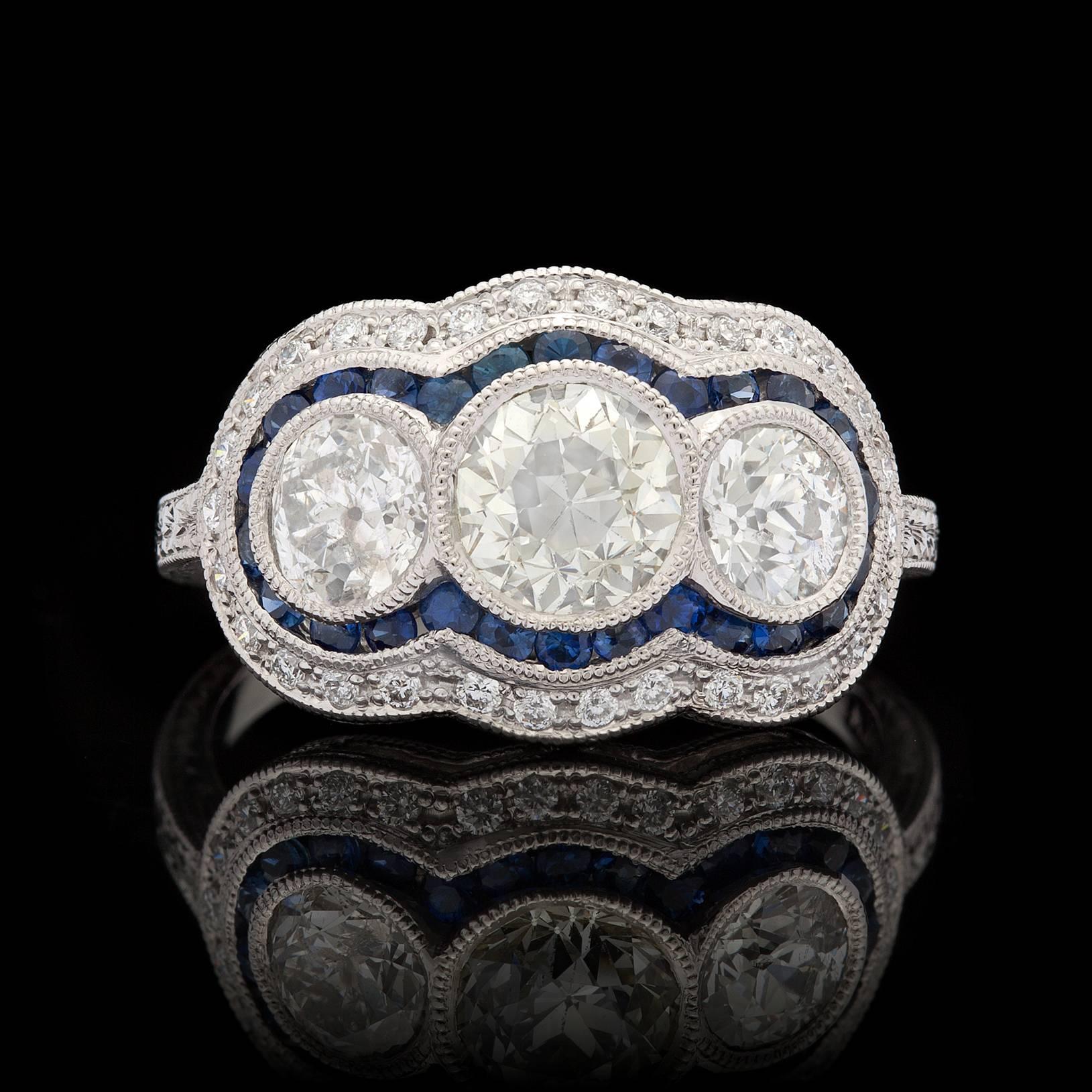 Custom platinum diamond Edwardian style ring features three old mine cut diamonds for approximately 1.82 ct. tw. with a lovely border of 26 blue sapphires and 30 additional round cut diamonds. The total carat weight for the additional 30 diamonds is