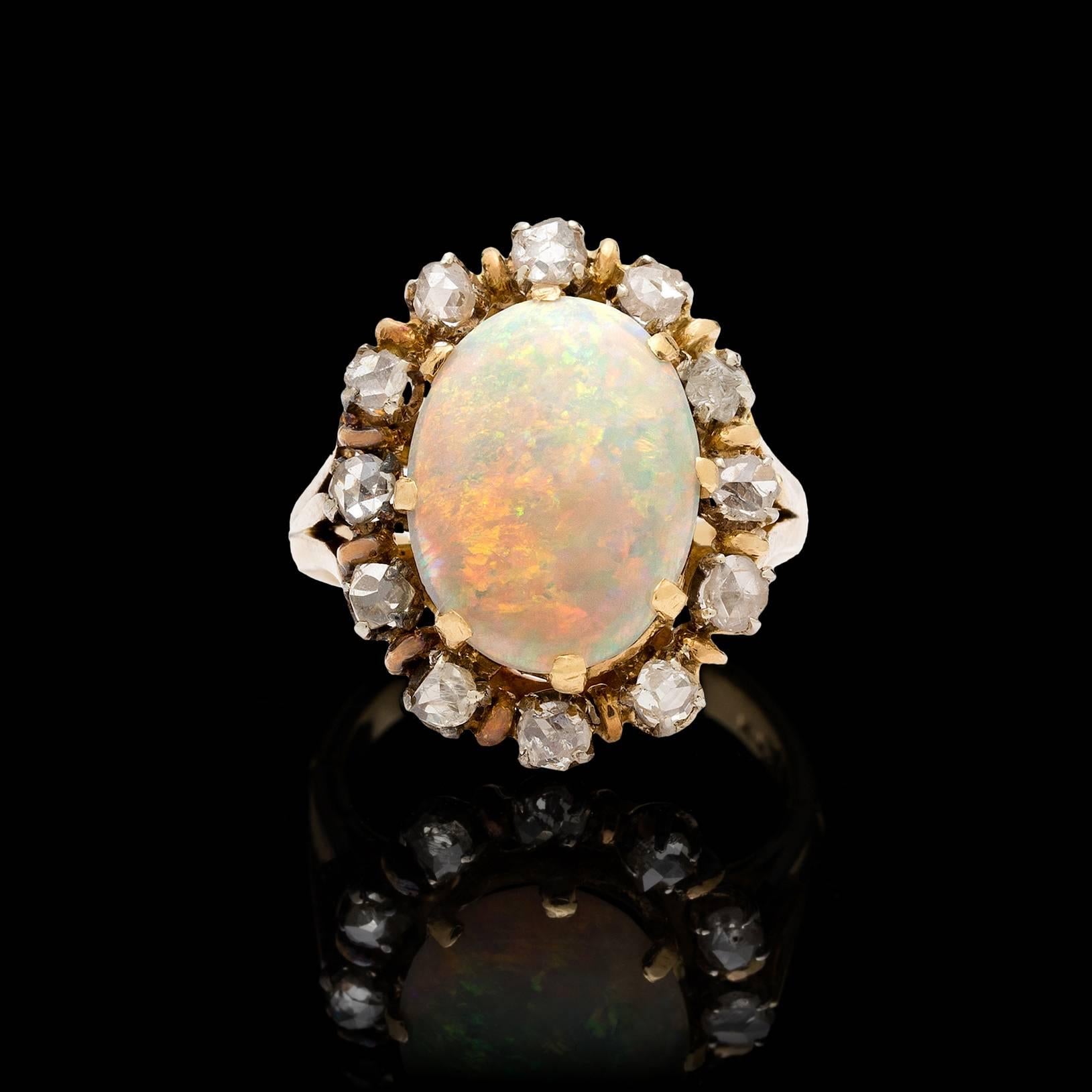 Vintage 18k yellow gold ring features a white opal with a play-of-color flashes of red, blue, & green in a pinfire pattern. The opal measures 13.5 x 10.5 x 3.4 mm. Surrounding the opal are 12 rose cut diamonds totaling approximately 0.50 carats.
