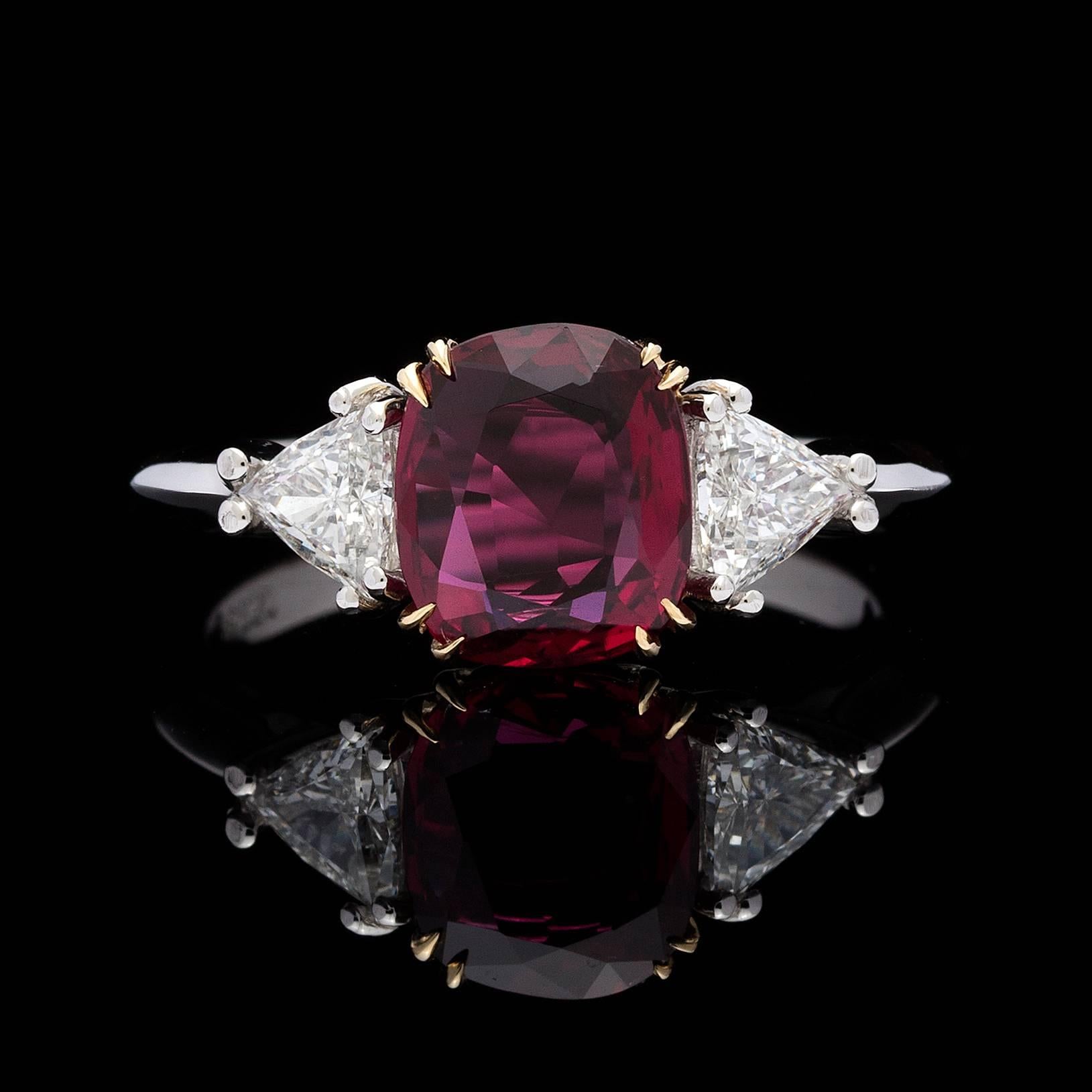 18k white gold ring features an AGL 2.04 carats cushion cut purplish-red ruby. Flanked on each side are brilliant trillion diamonds totaling 0.46 carats. The center ruby is set in yellow gold split-prongs and diamonds set in white gold split prongs.