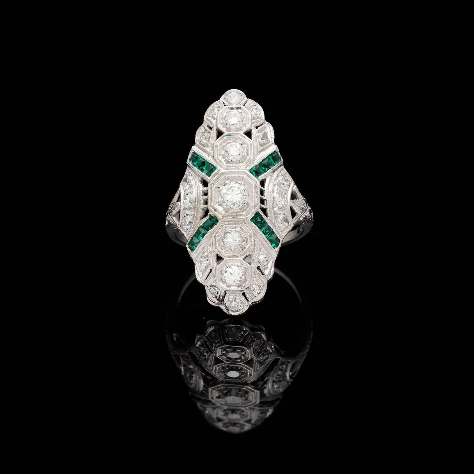 Deco platinum north south style ring set with 5 round transitional cut diamonds totaling 0.70 carats. Accenting the ring are melee size single cut diamonds and synthetic emeralds which are indicative of this period piece. The top of the ring