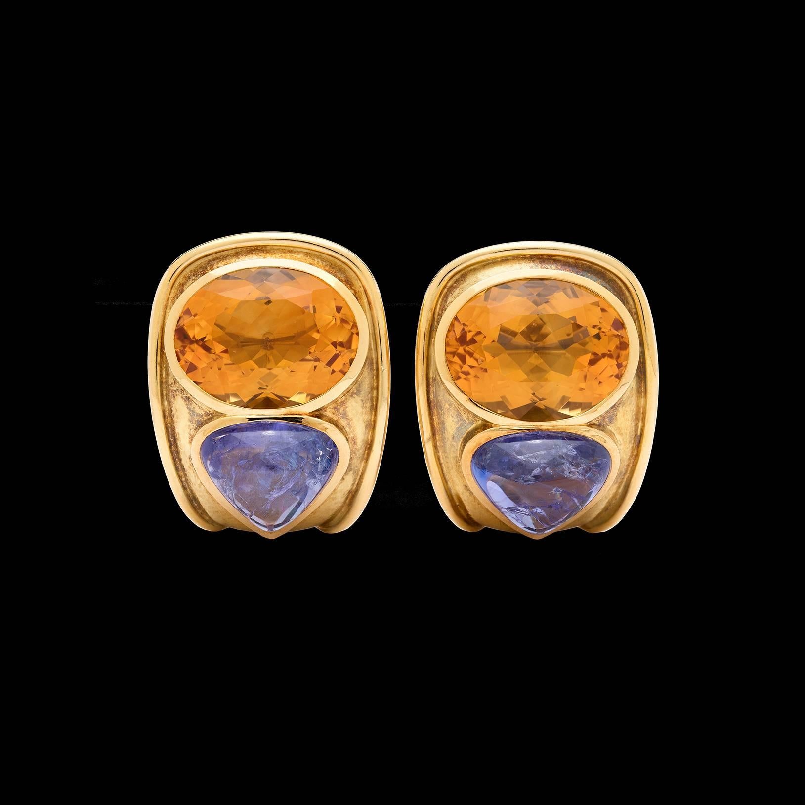 Bold and colorful estate De Vroomen 18k yellow gold clip back earrings from London. These fantastic earrings feature two large oval cut citrine quartz bezel set alongside two cabochon tanzanites. The earrings measure 1 1/8 inch long by 1 inch wide