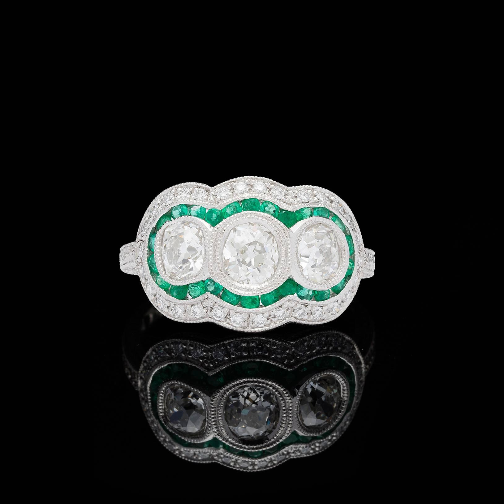 Three re-purposed antique old mine cut diamonds totaling 1.34 carat (J-K & VS-SI) set in an intricate platinum Edwardian style custom setting. A halo of 27 round cut emeralds in a vibrant green color accentuate the stones along with an additional 30