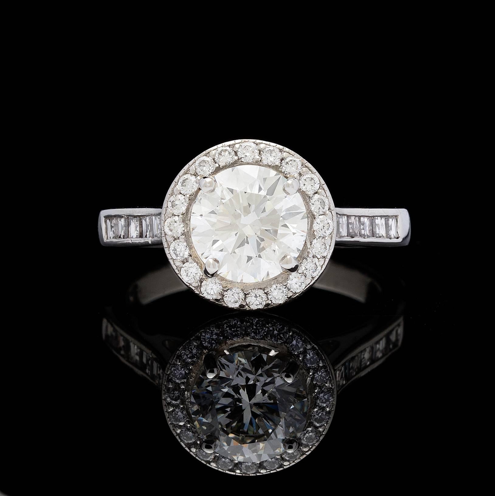 Bague en platine présentant un diamant rond de taille brillant H/SI1 de 1,57 carat, certifié par le GIA, dans un halo de diamants ronds de taille normale.  L'anneau est serti de diamants taille baguette, ce qui crée un joli contraste.  Les diamants