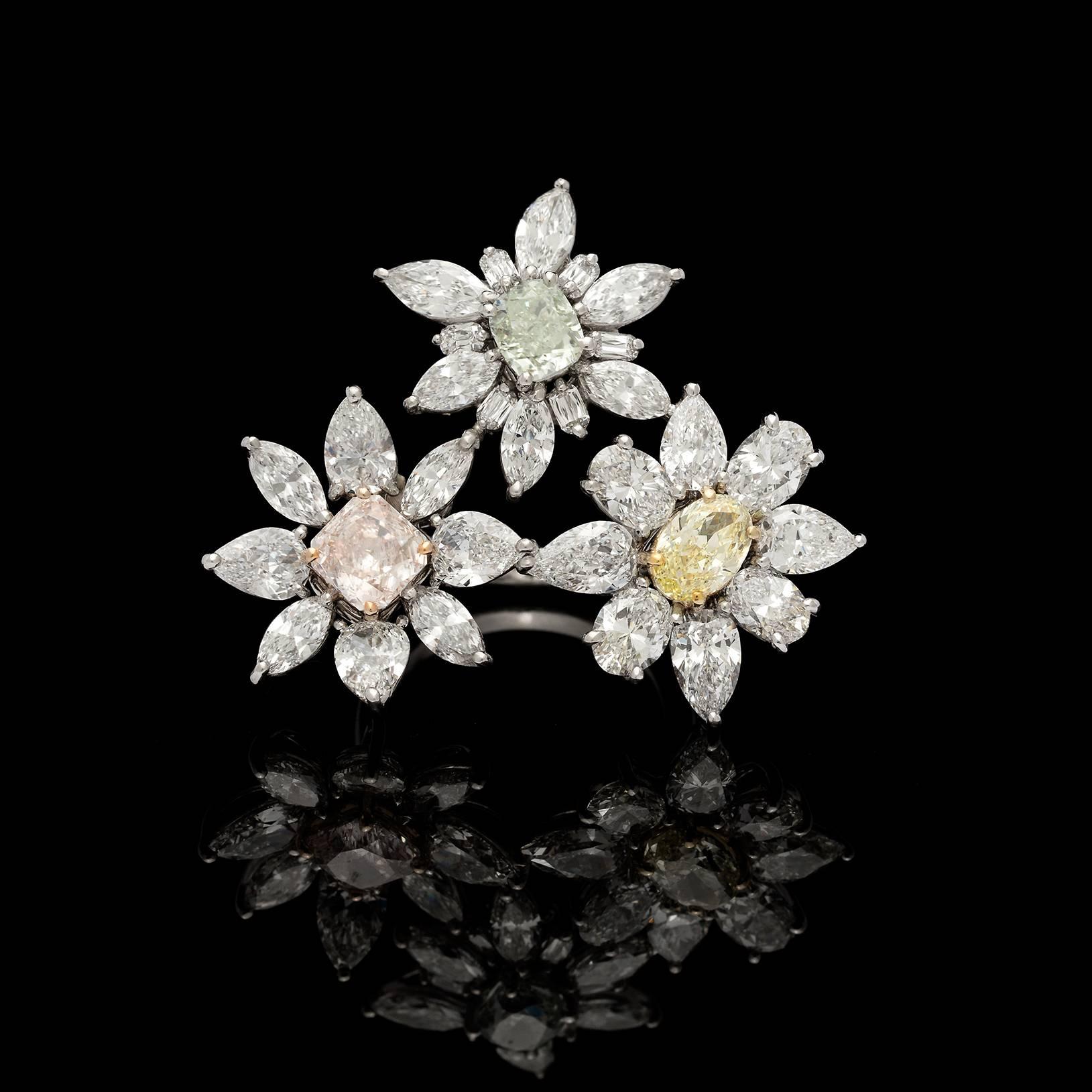 This eye-catching platinum ring is designed with three flowers, each showcasing a rare Fancy Colored Diamond (a GIA 0.84-ct. fancy light yellow oval-shaped diamond, an IGI 1.09-ct. fancy light pink radiant-cut diamond, and a GIA 0.95-ct. fancy light