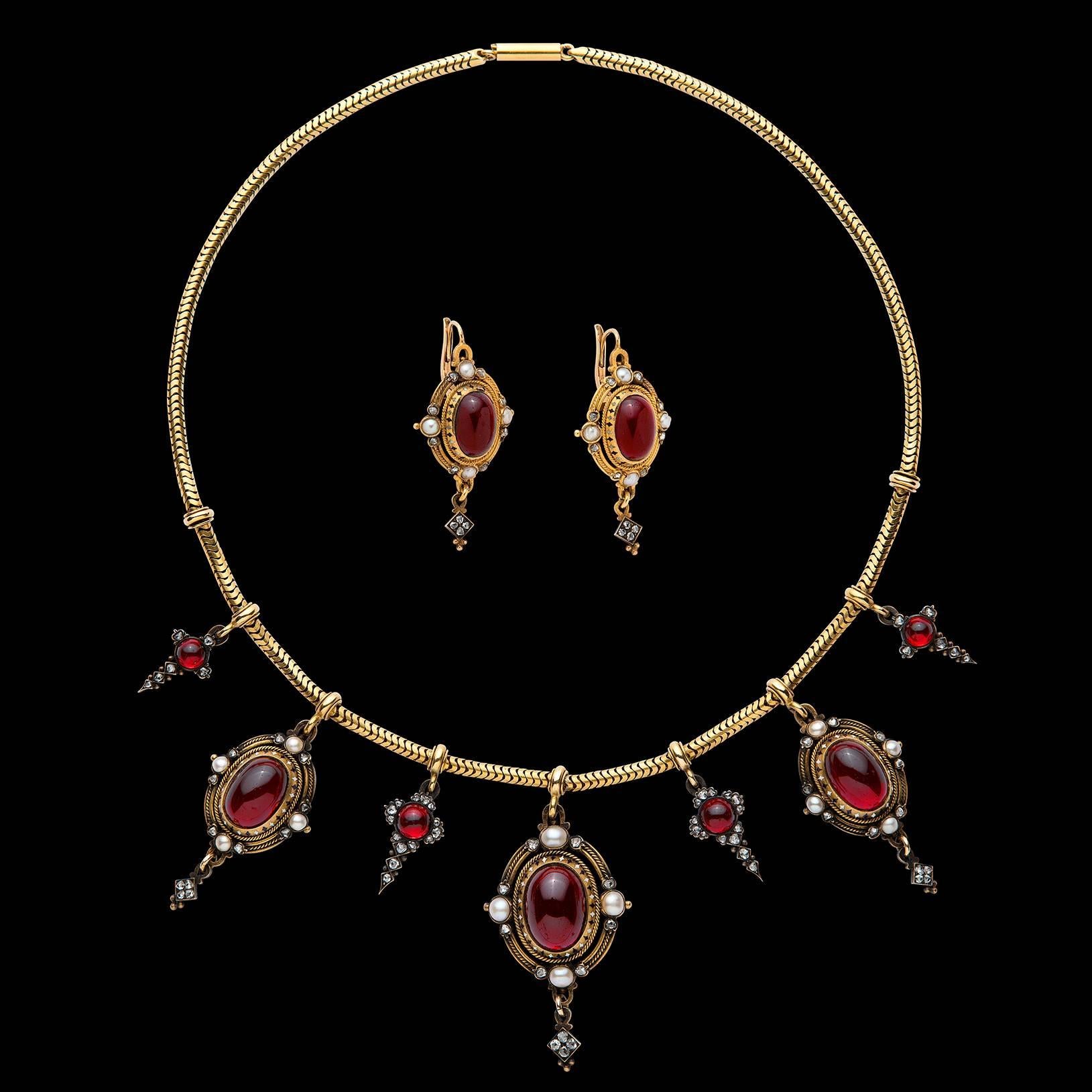 A prime example of Holbeinesque Jewelry, this incredible piece of history features matching necklace and earrings highlighting over 32 carats of phenomenal cabochon garnets set amidst 100 Rose Cut Diamonds and accent pearls. The total weight of this
